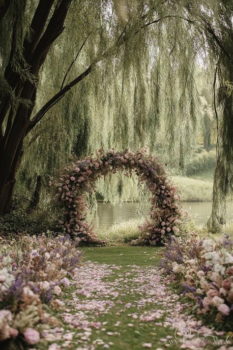 Floral archway by a tranquil pond under lush trees. Unearth a treasure trove of vibrant and whimsical ideas to sprinkle your spring wedding with the season’s unique charm and charisma. Outdoor Fairy Wedding Ideas, Wedding Under Weeping Willow Tree, Ethereal Wedding Arch, Forest Fairy Wedding Theme, Spring Fairy Wedding, Pond Wedding Ideas, Moongate Wedding, Garden Wedding Ideas Elegant, Pond Wedding Ceremony