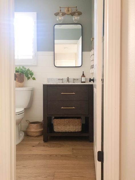 Small half bathroom with white shiplap halfway up the wall, dark single sink vanity with light marble top, polished nickel and brass fixtures, black rectangle mirror above vanity. Half Bath With Dark Vanity, Small Bathroom Single Vanity, Dark Vanity Small Bathroom, Bathroom Remodel With Dark Cabinets, Main Level Half Bathroom Ideas, Dark Vanity Powder Room, Half Bathroom Ideas With Window, Dark Brown Bathroom Vanity Ideas, Transitional Half Bathroom