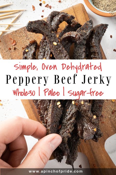 Hand grabbing a slice of peppery beef jerky. Jerky is on a wooden board sprinkled with red pepper flakes and ground pepper. There are a few toothpicks on the top left. Tag says "Simple, Oven Dehydrated Peppery Beef Jerky. Whole30, paleo and sugar-free." Simple Jerky Marinade, Jerky Marinade Recipes, Beef Jerky Recipe Dehydrator, Beef Jerky Marinade, Jerky Recipes Dehydrator, Jerky Marinade, Smoked Beef Jerky, Best Beef Jerky, Venison Jerky