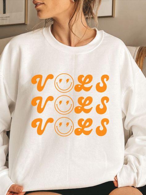 Your new Tennessee Game Day go-to.

VOLS with a lightning smiley printed retro style on the coziest heavy blend crewneck sweatshirt in Tennessee orange.

For an oversized fit, order 1-2 sizes up!

These garments are made from polyester and cotton. This combination helps designs come out looking fresh and beautiful. The collar is ribbed knit, so it retains its shape even after washing. There are no itchy side seams on these sweaters. Tennessee Vols Shirts Vinyl, Tennessee Vols Outfit, Tennessee Game Day, Tennessee Vols Shirts, Tennessee Sweatshirt, Preppy Orange, Tennessee Orange, Tennessee Vols, White Crewneck Sweatshirt