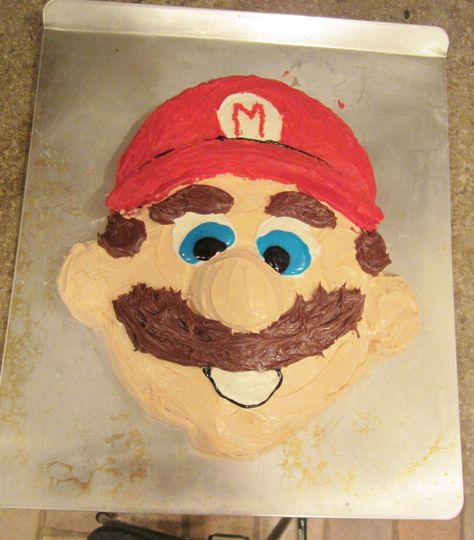 Use two 9" rounds and 3 cupcakes. Use one 9" round for the face and then cut the other to shape for the hat.  Use 3 cupcakes for the nose, ears and chin.  I think it turned out pretty cute! You'll have to buy the red, blue, black and brown frosting's, but you can make the flesh color one for the face by mixing 8 drops yellow, 6 drops red, 2 drops green into a vanilla can of frosting. Mario Face Cake, Mario Face, Colored Frosting, Themed Baking, Face Cake, Flesh Color, Coloured Icing, Bday Cake, Mario Party