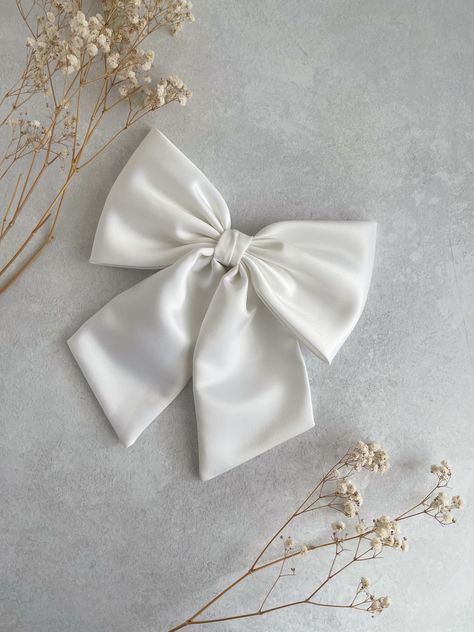 Large and Luxurious White Duchess Satin with tails hair bow.  This oversized hair bow is an ideal hair accessory for wearing to a special occasion, absolutely perfect as bridal hair bow for a wedding, hen party or evening reception!  It will also make a great "gift for girl." They are handmade with love and care from  high quality fabric in our studio in England. The bow measures  8" in width appx  12 cm or 4 3/4" in height  Tail is 18 cm or 7" long approximately  📍Attachments :  ✅Barrette  ✅Co Black Zip Up Hoodies, Bridal Bow, White Hair Bow, Large Hair Bow, Evening Reception, Giant Bow, Disney Bows, White Hair Bows, Large Hair Bows