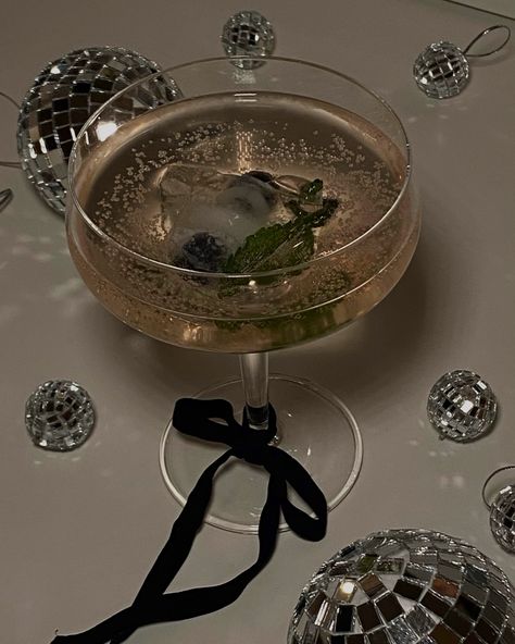 cocktail glass with black bow around the stem surrounded by discoballs Black Cocktail Aesthetic, Glitter Drink Aesthetic, New Years Eve Mocktail, Sparkly Cocktails, Soiree Aesthetic, Disco Cocktails, New Year’s Eve Aesthetic, Mocktails Aesthetic, Xo Party