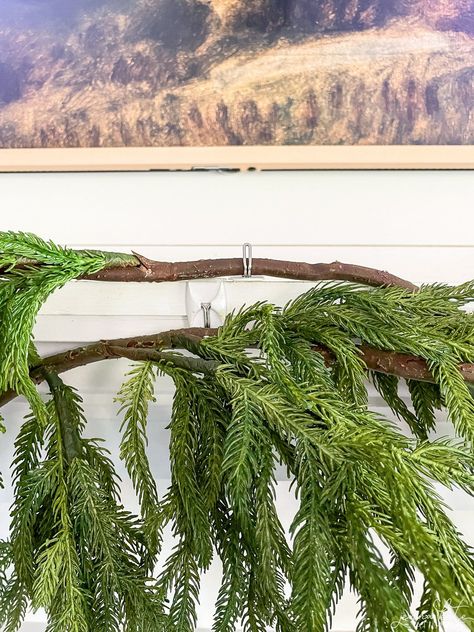 Learn the best tips and tricks for hanging garland on your mantel this Christmas. Hanging Garland On Mantle Fireplace Mantels, Garland Hanging Ideas, White Pine Garland Decorating Ideas, Hanging Garland On Wall, Garland Hanging Hack, Cedar Garland Christmas Mantle, Making Cedar Garland, Christmas Mantel Garland Grandin Road, Attaching Garland To Mantle