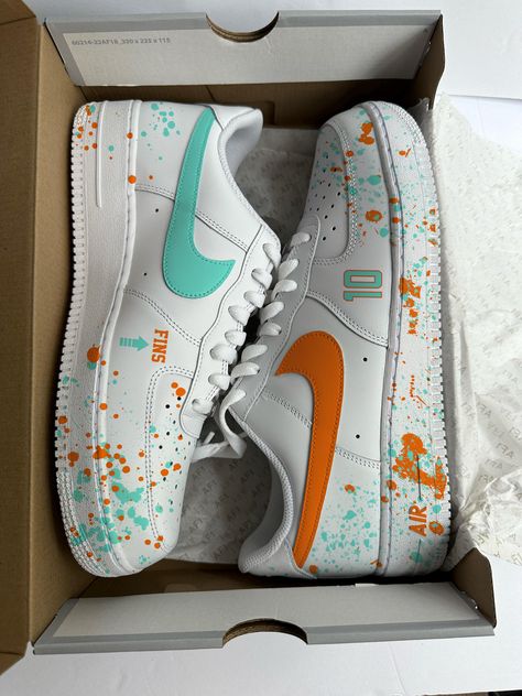 PLEASE ALLOW 7 TO 10 BUSINESS DAYS FOR CUSTOMIZATION PRIOR TO SHIPPING. ALSO, THE COLOR MAY VARY SLIGHTLY DEPENDING ON LIGHTING AND SCREEN RESOLUTION. LASTLY THE PAINT SPLATTER WILL VARY AS THESE SHOES ARE MADE TO ORDER Step up your sneaker game with these custom Miami Dolphins-inspired Air Force Ones! This unique pair combines high-quality paint and precision decals to showcase the vibrant teal, orange, and white color scheme that represents the Dolphins spirit. Whether you're tailgating at Hard Rock Stadium or simply repping your team on the streets, these sneakers are the perfect way to display your Dolphins pride. Hard Rock Stadium, Custom Af1, Air Force 1 Custom, Custom Air Force 1, Hand Painted Shoes, Leather Paint, Custom Football, Teal Orange, Sneaker Games