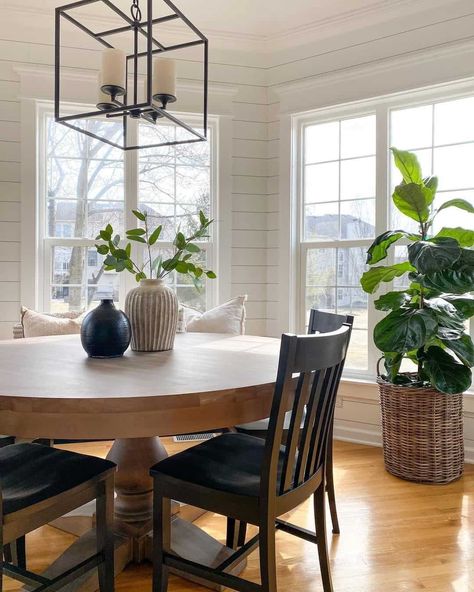 A modern cube chandelier is suspended from the ceiling of this shiplap dining room. Round dining table centerpieces include two vases in contrasting colors placed on a wood pedestal table. Wooden dining chairs surround the table...   Image: athomeontheboulevard Shiplap Dining Room, Round Kitchen Table And Chairs, Farmhouse Round Dining Table, Wood Pedestal Table, Round Dining Table Decor, Dining Table Centerpieces, White Round Dining Table, Breakfast Nook Table, Nook Table