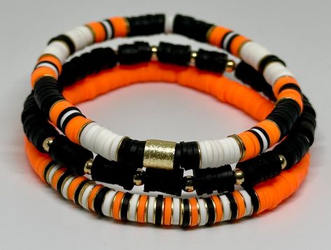 Set of 3 Black Orange and White, hand beaded, stretch bracelets. Each strand is made with 6mm Heishi beads with gold accents. Can be customized with team or wording of your choice. Lettering options include white/black letters, black/white letters, and white/gold letters. Bengals Bracelets, Bracelets Stacking, Black And White Football, Clay Bracelets, Boys Bracelets, Holiday Bracelets, Making Bracelets With Beads, Autumn Bracelet, Halloween Bracelet