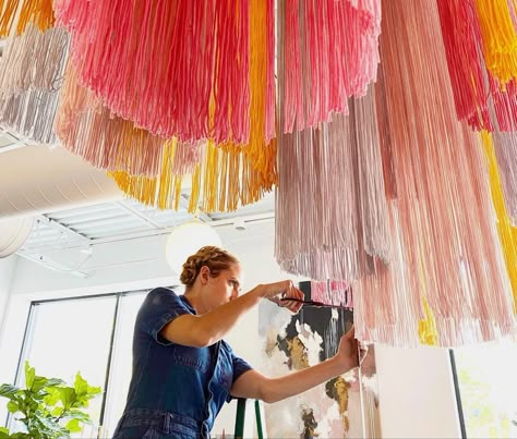 Luci trimming yarn hoops. Ceiling installation Fringe Chandelier Wedding, Tassel Ceiling Decor, Fabric Ceiling Installation, Fringe Hanging From Ceiling, Ribbon Ceiling, Yarn Installation, Fringe Chandelier, Ceiling Art Diy, Hanging Installation