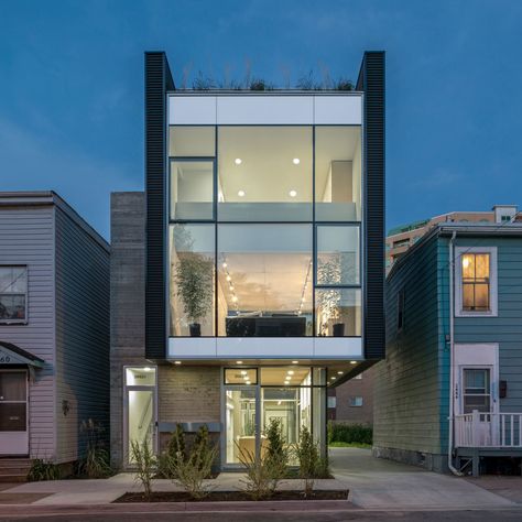 The home’s front façade features an anodized aluminum and glass curtain wall by Kawneer that's framed by Vic West black corrugated metal panels. The board-formed concrete on the exterior enables passive solar absorption, allowing optimal heat retention on cold winter days. The metal and concrete exterior cladding offers cohesive dialogue with the neighboring industrial sheds and commercial buildings. Shop Houses, Live Work Space, Decoration Details, Interior Vintage, Narrow House, Glass Walls, Rooftop Garden, Design Exterior, Facade Design