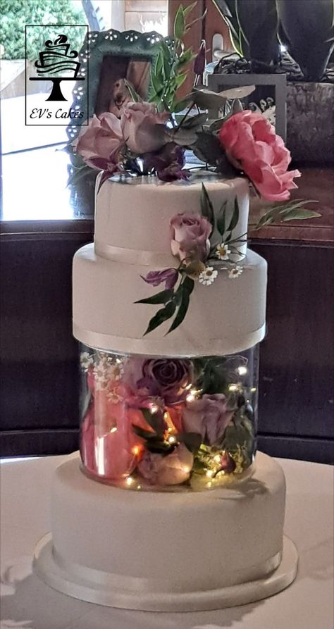 Plain white iced wedding cake with fresh flowers and fairy lights Cake With Lights Inside, Cakes With Lights, Fresh Flower Wedding Cake, Cake With Lights, Enchanted Forest Wedding Cake, Azalea Wedding, Iced Wedding Cake, Wedding Cake Forest, Wedding Cake With Fresh Flowers