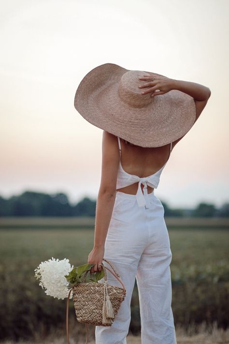 Annie B. standing in field watching sunset in oversized straw hat and white linen jumpsuit taken from behind Outfit With Straw Hat, Woman From Behind, Swimsuit Shoot, White Linen Jumpsuit, Girls Wearing Hats, Watching Sunset, Open Dress, Linen Jumpsuit, Straw Hats