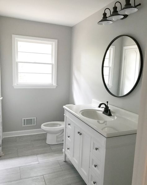 White and gray bathroom with black circle mirror. White cabinets with black hardware. White Cabinets With Black Hardware, Black Circle Mirror, White And Gray Bathroom, Cabinets With Black Hardware, Bathroom Inspiration Grey, Light Grey Bathrooms, Blue Bathrooms Designs, Grey And White Bathroom, Gray And White Bathroom