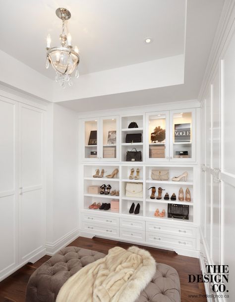 Glam closet features tray ceiling accented with a glass and nickel chandelier with crystal droplets illuminating a brown velvet tufted ottoman flanked by built-in wardrobe cabinets. The back of the walk-in closet boasts glass front display cabinets filled with designer bags illuminated by custom lighting stacked over cubbies filled with shoes and storage drawers accented with glass pulls. Dream Closet Design, Walk In Closet Design, California Closets, Closet Renovation, Closet Decor, Dream Closets, Room Closet, Closet Inspiration, غرفة ملابس