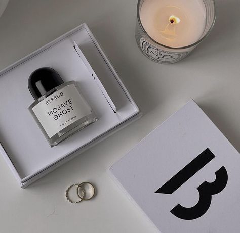 A perfume bottle still in the box, a candle, and two gold rings. Perfume Ig Feed, White Aesthetic Perfume, Perfume Black And White Aesthetic, Perfume Minimal Photography, Black Saffron Byredo, Mojave Ghost, Perfume Packaging, Aesthetic Design, Instagram Aesthetic