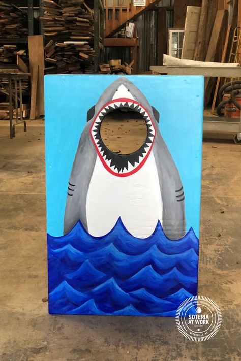 Our interns built miniature versions of our cornhole boards, and staff painted them to look like sharks jumping out of the water to grab the cornhole bag! Bags sold separately, but sewing a set in the shape of fish would make this game even more imaginative for kids! Cute Cornhole Boards, Cornhole Designs Paint, Painting Cornhole Boards Designs, Corn Hole Boards Designs Ideas, Painting Ideas For Corn Hole Boards, Cornhole Boards Designs Diy Paint, Shark Bean Bag Toss, Pirate Cornhole Boards, Cornhole Board Designs