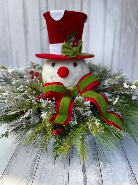 A sweet and traditional looking centrepiece contains a large snowman head and co-ordinating bow. The centerpiece is full of many different styles of faux mixed pines, frosted ferns, greenery and berries. This piece will last the decades of tradition as a fantastic table or hallway entry centerpiece. Snowman Head Centerpiece, Snowmen Crafts, Skeleton Wreath, Christmas Sweet Treats, Snowman Head, Hallway Entry, Family Decor, Snowman Crafts, Christmas Truck