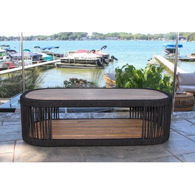 This coffee table completes your outdoor living room with a breezy, coastal aesthetic. Its distinct oval frame is crafted from solid teak wood with a lower shelf below the table top - great for drinks, snacks, and extra throw blankets. The design features black natural rope woven around the edges and on either end that gives it a dynamic look. We love that this coffee table has such a beach-y and organic vibe, but it's also resistant to water, UV rays, and rust. | Beachcrest Home Tena Outdoor Co Thanksgiving Mantel Decor, Outdoor Seating Set, Coastal Aesthetic, Outdoor Coffee Table, Teak Coffee Table, Outdoor Bar Stools, Outdoor Side Table, Outdoor Living Room, Black Rope