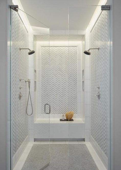 Facing each other, polished nickel shower heads are mounted to a white and gray herringbone backsplash framed by white border tiles that also accent gray grid floor tiles. Double Shower Head Master Baths, Hay Interior, Grey Bathroom Wall Tiles, Double Showers, French Style Architecture, Gray Bathroom Walls, Magic Attic, Bathroom Green, Gray And White Bathroom