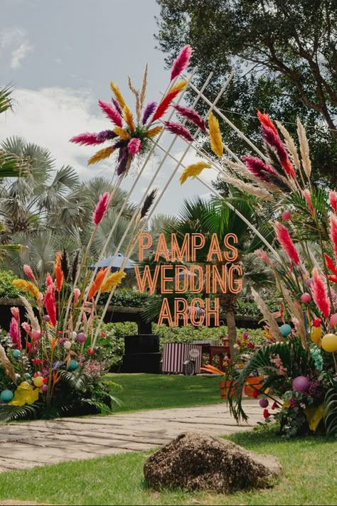 From reception of your guests to the smallest details in your bouquet, pampas grass can make a big impact on the boho vibe of your special day. With all the bright colors offered, it puts a spring step into the wedding entrance. Boho Decor Wedding Inspiration, Colorful Wedding Entrance, Colorful Boho Wedding Decor, Guest Entrance Wedding, Boho Theme Mehendi Decor, Flower Entrance Decoration, Boho Wedding Entrance, Boho Mehendi Decor, Boho Mehendi