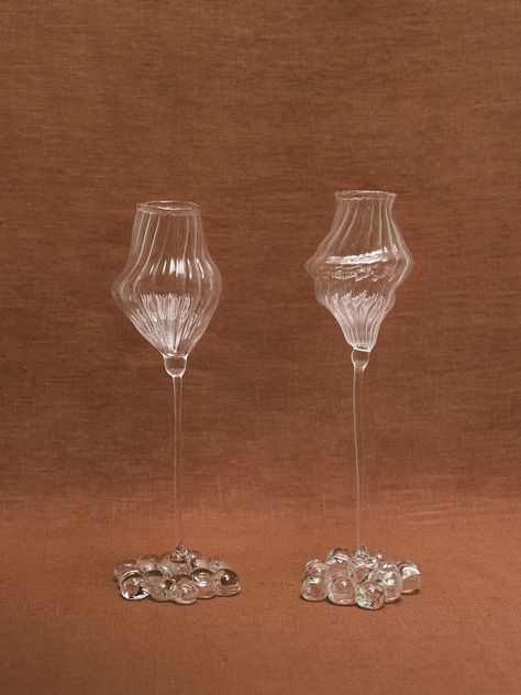 On a brown surface, two exquisite Orphée Liqueur Glasses from Justine Menard are showcased. These tall, mouth-blown glasses feature unique artistic forms with a textured and wavy design. Each handmade piece rests on a base embellished with multiple glass pebbles. The background is draped in a matching brown fabric that enhances the overall aesthetic. Making Centerpieces, Elegant Candle Holders, Organic Sculpture, Liqueur Glasses, How To Make Drinks, Table Cafe, Bar Supplies, Bowl Designs, French Design