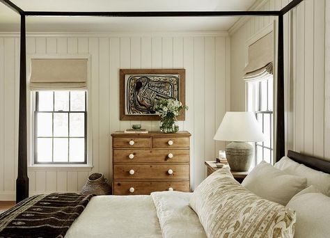 Cottage style bedroom features a brown farmhouse dresser with white knobs on vertical tongue and groove trim and black canopy bed lit by a gray lamp. Colonial House Bedroom, Tongue And Groove Walls Bedroom, Tongue And Groove Bedroom, Vermont Cabin, Dark Grey Curtains, Shiplap Bedroom, Black Canopy Bed, Gray Lamp, Cottage Style Bedroom