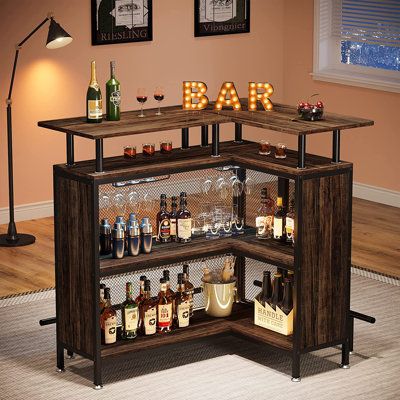 This corner bar cabinet is space-efficient and stylish, providing an all-in-one solution for your home bar needs. With a 2-tier storage system, it can hold dozens of spirits and mixers, while the built-in stemware racks accommodate up to 12 wine glasses or champagne flutes. The large desktop lets you enjoy drinks and celebrate events with friends, and the second shelf helps reduce clutter during gatherings. Its elevated design is compatible with taller chairs, while the footrests add extra comfort while you sip your cocktails. Crafted with metal mesh to prevent bottles from falling, this bar cabinet is designed for small gatherings, dinner parties, and holiday events. Wade Logan® Color: Brown | Wade Logan® Bhima Bar Unit w / Storage 41.93 H x 47.24 W x 35.43 D in black / Wood in Brown | 41 Home Bar Unit, Free Standing Bar, Bar Table Design, Mini Bar At Home, Corner Bar Cabinet, Apartment Bar, L Shaped Bar, Shelves Corner, Corner Bar