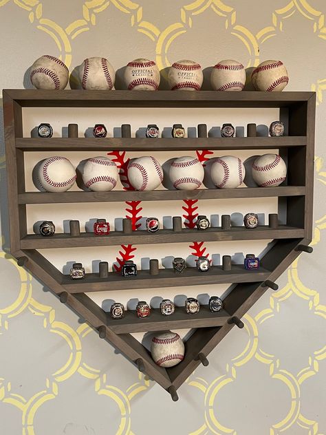 "Take your baseball players room to the next level with this custom crafted Homeplate Baseball and Ring display case. Trophies are out and rings are in! Help him/her show off their accomplishments with this beautiful keepsake that can travel with them throughout each move. This case is approximately 24\"x24\"x 3 3/4\" deep. The one shown has a red mahogany stain on white pine. It will hold 12 regulation size baseballs and 33 rings. (Not included.) We can add a two digit max personalization in th Baseball Ring Holder, Dads Office, Baseball Themed Bedroom, Baseball Project, Home Plate Baseball, Baseball Holder, Ring Display Case, Baseball Ring, Trophy Shelf