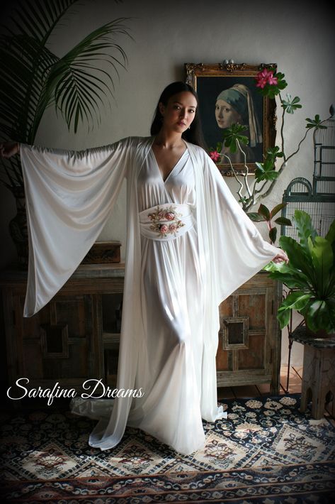 "White satin Bridal robe from our newest collection. Our satin is a stretch poly nylon that is the softest you'll find both inside and out so the fabric next to the skin is slinky and very silky. This is a match to our angel wing gown and is graced with long pointed wing sleeves. A classic kimono style that we've added a train to which adds a touch of glam and romance. Two side inseam pockets and it will come with a self fabric tie sash belt to close. It is shown with the angel wing gown which i Angel Lingerie, Winged Sleeves, Wedding Sleepwear, Moda Kimono, Satin Bridal Robe, Vintage Loungewear, Night Gown Dress, Bridal Nightgown, Robe Wedding