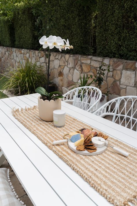 Create your own outdoor Hamptons space with our 5 easy tips. Hamptons design style is an increasingly popular style. With this stunning white outdoor dining table, subtle striped jute table runner, white orchid, white wicker chair, white orchid, and of course this gorgeous round cheese board. For more ideas to help you achieve a Hamptons look, click on the pin or go to StyleCurator.com.au. Outdoor Patio Ideas Table And Chairs, White Outdoor Dining Tables, White Metal Outdoor Table, Outdoor Dining Styling, Outdoor Dining Table Styling, White Outdoor Dining Chairs, White Outdoor Dining Set, Outdoor Table Styling, White Patio Table