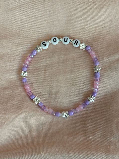 A hand-crafted glass bead friendship bracelet highlighting Olivia Rodrigo's album, SOUR! A simple and cute way to show off your favorite song or a great concert accessory!  This bracelet is made with Czech glass beads, plastic letter beads, plastic spacer beads, and is on an elastic thread measured at about 10 inches in length for a relaxed/loose fit. If you would like the bracelet you order to be smaller or larger, please leave the requested size in inches in the personalization box!  All bracelets are made to order and are typically shipped out within 1-3 business days unless otherwise stated. Olivia Rodrigo Sour Bracelet, Olivia Rodrigo Friendship Bracelet, Olivia Rodrigo Bracelets, Olivia Rodrigo Bracelet, Swiftie Bracelets, Bead Friendship Bracelet, Beaded Braclets, Plastic Letters, Friendship Bracelets With Beads