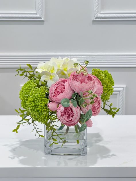 This premium lovely flower arrangement design includes  finest silk peonies, real touch hydrangea and green berries  filled with faux water in glass vase. This elegant arrangemenr can bring nature inside and brighten your space, especially for small tables at home, vanity tray, book shelf, small night stand, end table or office desk. FLOVERY™ takes pride in designing realistic and high-quality artificial flowers. Each flower is made with our real touch technology, giving them a natural look and Peony Arrangement Ideas, Real Flower Arrangements, Table Flower Decorations, Water In Glass, Peony Flower Arrangements, Hydrangea Green, Desk Flowers, Peony Arrangement, Shelf Small