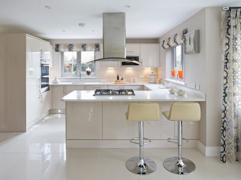 Sleek, modern minimalism informs the look of this kitchen, with expanses of glossy white in every direction. The large format tile flooring pairs well with white countertops and cabinetry, providing space for a pair of bar stools at the extended countertop in the foreground. Elegantly textured but transparent drapes add a healthy dose of visual complexity to the monolithic room. Kitchen Layout U Shaped, G Shaped Kitchen, Kitchen Design Images, Kitchen Layout Plans, Kitchen Design Color, Small Kitchen Layouts, Kitchen Modular, U Shaped Kitchen, Kitchen Designs Layout