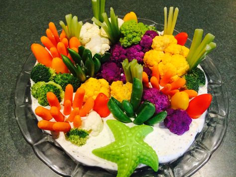 This is a coral reef veggie tray that I created for my granddaughter's mermaid birthday party.  I created the "sand" from two blocks of cream cheese mixed with a packet of ranch dip mix.  I stood carrots and snap peas on end and then cut celery several times lengthwise to make celery fans.  Small sweet peppers became rocks and smooth coral. Broccoli and several colors of cauliflower became coral. This was easy and fun to make and a real hit at the party. Ocean Veggie Tray, Under The Sea Veggie Platter, Coral Reef Veggie Tray, Ocean Themed Veggie Tray, Mermaid Veggie Tray, Under The Sea Charcuterie Board, Mermaid Food Ideas Kids, Mermaid Food Ideas, Ocean Party Food