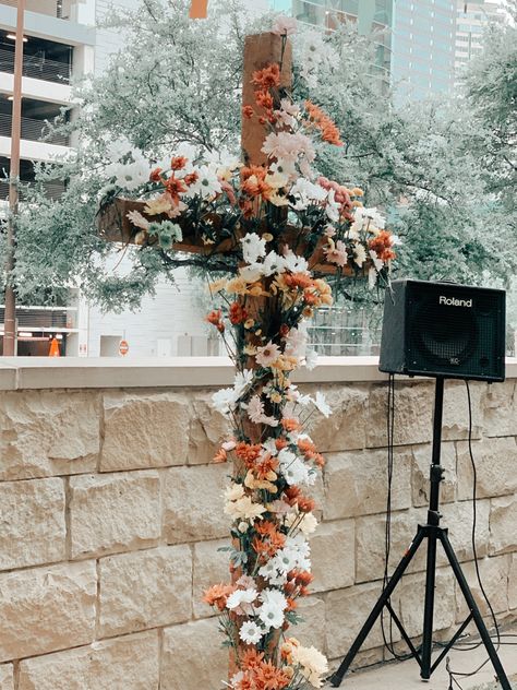 a wooden cross with different colored flowers stuck in it. it has a speaker in the back ground of it Flowers On A Cross Wedding, Flowers On Cross, White Flowers On Cross Wedding, Floral On Cross Wedding, Cross Floral Arrangements Wedding, Cross Floral Arrangements, Cross Alter With Flowers, Cross Flowers, Cross With Flowers