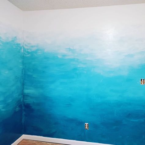 Deep ocean blue and pure white paint. Start with blue at the bottom (can roll on). Mix a lil white with blue in a tray and continue up the wall until about 2 ft from the top. Then use brush over entire wall to blend and make water like ripples. After blues are dry, start at top with pure white and blend down with brush! Beach Theme Wall Paint, How To Paint Waves On A Wall, Ocean Themed Accent Wall, Sea Wall Painting Ideas, Ocean Wall Colors, Diy Ocean Wall Painting, Ocean Ombre Wall, Wave Wall Painting Diy, Ocean Wall Painting Bedrooms