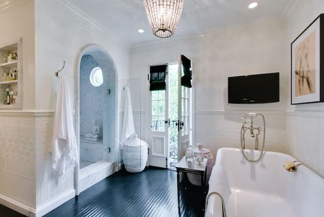 Master bath features flatscreen TV situated in front of freestanding bathtub paired with vintage style tub filler across from cave like shower with arched doorway, marble surround and Buddha next to French doors dressed in black roman shades illuminated by beaded chandelier. | Abbott Moon Shower Cave, Master Bathtub Ideas, Hollywood Bathroom, Bath Shower Combination, Arched Entry, Arched Doorway, Mediterranean Bathroom, Tile Backsplash Bathroom, Tv In Bathroom