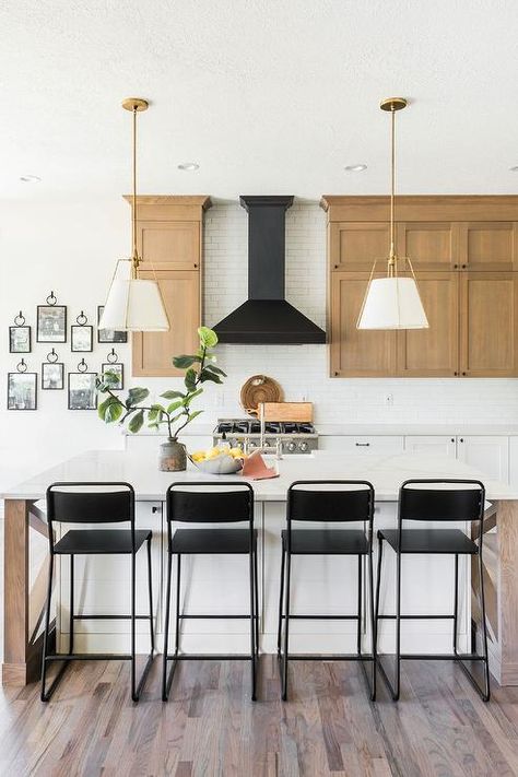 Black counter stools sit at a  white and brown kitchen island lit by white hanging shade pendants and finished with a sink fitted to a white quartz countertop. Oak Cabinet Kitchen, Cabinet Kitchen Island, Kitchen Island Chairs, Natural Wood Kitchen Cabinets, Wood Hood, Cherry Wood Kitchens, Outdated Kitchen, Farmhouse Makeover, Black White Home