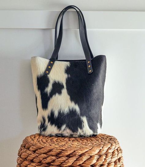 Add a western element to your look with this unique cowhide tote topped with soft leather handles. Hand-crafted by artisans in Kenya. Due to the handmade nature of this item, there will be variations in hides.
16" W x 13" H x 6" D
Strap drop: 10"
Made of leather and cowhide
Interior pocket
Leather is treated to ensure hair does not come off
Do not machine wash or dry clean. Wipe bag with a damp cloth using a mild soapy solution.
Made in Kenya
Please note, we cannot offer refunds on candles, ceramics, glassware, napkins, and final sale products.
Click here to view our full Return Policy. Cow Purse, Cow Print Bag, Senior Year Of College, Western Embroidery, Cowhide Purse, Cowhide Bag, Summer Tote, Diy Purse, Chic Gifts