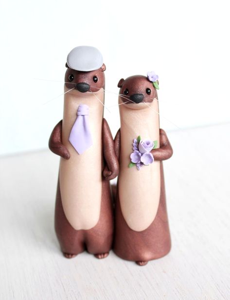 This River Otter wedding cake topper is meticulously hand sculpted from polymer clay, enhanced with mica mineral powders for a subtle pearly shine and an elegant marble effect. The otter groom is adorned with a flat cap and tie, while the bride is beautifully decorated with lilac flowers. Each piece is handmade to order, ensuring your river otters are truly one of a kind. Variations in facial expressions, head tilts, and body curves create unique characters every time. Personalize your topper by choosing different types and colors of flowers to perfectly match your wedding theme, maintaining a unique and human-like charm while staying true to the original design. Otter Wedding Cake Topper, Clay Otter Diy, Cute Wedding Cake Topper, Wedding Cake Topper Ideas Unique, Clay Otter, Otter Wedding, Fox Cake Toppers, River Otters, Strawberry Mochi