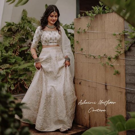 Ashwini Mathoor on Instagram: "An exquisite lehenga in a snowbound color, completed with a lustrous silk blouse with beautiful hand - embroidery and a flattering silhouette. The timelessness of Beauty❤ D Gorgeous Bride Meenu swoon under the spell of an off-white banarasi lehenga paired with blouse handembroidered using zari and sequins. The lehenga is a wonder.😍 The bridal edit is exquisitely constructed using the finest fabrics and the most detailed finishings. #signaturelehenga #AshwiniMa Off White Traditional Dress, Off White Banarasi Lehenga, Bridal Lehenga Kerala, Save The Date Dress Kerala, Maduramveppu Dress Kerala, Banarasi Bride, Hindu Engagement Dress Kerala, Kerala Lehenga, Lehenga Styling