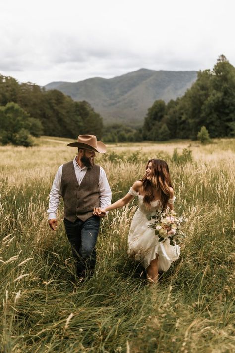 A bride and groom hold hands and smile at each other while walking through an overgrown field with the Great Smoky Mountains behind them on their elopement day Smoky Mountain Couple Photos, Smoky Mountains Elopement, East Tennessee Elopement, Gatlinburg Elopement Photography, Telluride Elopement Fall, Casual Mountain Elopement, Elopement Ideas Tennessee, Asheville Nc Elopement, Great Smoky Mountains Wedding