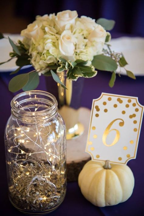 Wedding Centerpiece : White Roses, Eucalyptus, and White Hydrangeas. Fairy Light Mason Jar with Pumpkin Table Number Temescal Beach House Wedding. Oakland, CA Dianne Jones Photography #whitepumpkin #masonjar #fairylights #wedding #gold #purple #centerpieces #whitehydrangeas #whiteroses #eucalyptus Pumpkin Table Numbers Wedding, Pumpkin Table Numbers, Wedding Flowers White Roses, Volleyball Banquet, Wedding Flowers White, Purple Centerpieces, Wedding Centerpieces Mason Jars, Wedding Flowers Hydrangea, Lighted Centerpieces