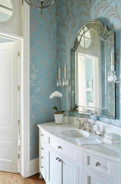 Silver and blue powder room features silver and blue metallic wallcovering lined with an arch venetian mirror lit by crystal droplets candle sconces placed over a white curved single washstand topped with white marble fitted with an oval sink and a polished nickel vintage faucet. Blue Powder Rooms, Blue Powder Room, Summer House Interiors, Powder Room Wallpaper, Silver Bathroom, Powder Room Decor, Powder Room Design, Powder Rooms, Trendy Bathroom