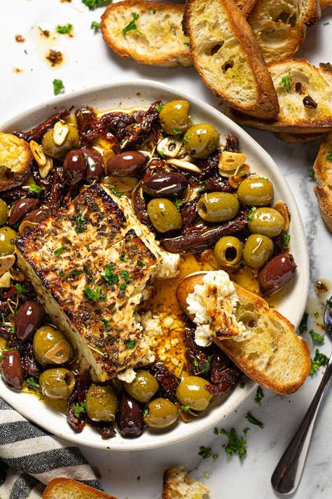 This Baked Feta Appetizer comes together in just minutes with only a handful of ingredients - olives, sun-dried tomatoes, fresh garlic, olive oil, and herbs. Bake it all together with a block of feta cheese until it's warm and creamy then serve with crispy crostini! Olives Appetizer, Crispy Crostini, Feta Appetizer, Mini Aperitivos, Baked Feta Recipe, Roasted Olives, Feta Cheese Recipes, Baked Feta, Feta Recipes