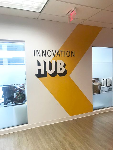 Yellow arrow with Inovation Hub lettering wall mural at a workplace Workplace Wall Design, Wall Paint Designs Classroom, Logo Wall Painting, Tech Mural Design, Creative Offices Workspaces, Wall Murals Office Work Spaces, Wall Painting Ideas For Office, Innovation Hub Design, Office Murals Workspaces