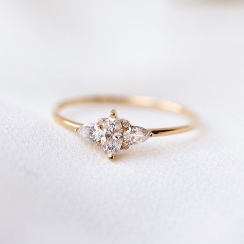 A striking array of diamonds makes this ring sparkle in the light. The 14k Delicate Marquise Cut Diamond Cluster Engagement ring features a marquise cut center diamond surrounded by selection of pear and round cut diamonds. Discover more sustainably sourced engagement rings at Local Eclectic. Simple Vintage Engagement Rings Round, Delicate Cluster Engagement Ring, Simple Engagement Rings Vintage With Band, Dainty Gold Engagement Ring Melanie Casey Fine Jewelry, Minimal Engagement Ring Rose Gold, Simpler Vintage Engagement Ring, Simple Engagemnet Rings, Delicate Diamond Engagement Ring, Simplistic Engagement Rings Rose Gold