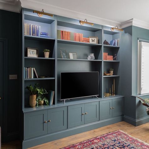 The Esher sitting room was given a library feel with bespoke cabinetry to house TV, books and ornaments. Inchyra Blue from @farrowandball… Book Case With Tv, Library With Tv, Blue Tv Wall, Bespoke Cabinetry Living Room, Library Wall With Tv, Bookshelves In Living Room With Tv, Dark Blue Feature Wall, Blue Bookshelves, Blue Cupboards