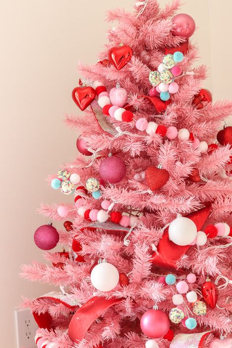 closeup of pink Christmas tree with red, white, and pink pom garland and red heart ornaments, pink glitter ornaments and white ornaments White Christmas Ornaments Aesthetic, Pink Peppermint Christmas Tree, Hot Pink Christmas Tree Decorations, Pink And Red Christmas Tree Decorations, Pink And Red Christmas Aesthetic, Pink Red And White Christmas Decor, Red Pink Christmas Tree, White Christmas Tree With Pink Ornaments, Pink Christmas Tree Aesthetic