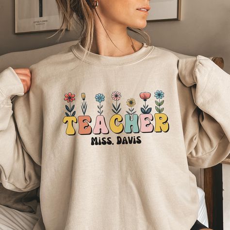 This sweatshirt features a beautiful floral design alongside a 'Teacher' logo, perfect for celebrating educators. It also offers a personalized touch, allowing you to add the teacher's name, making it a thoughtful and unique gift for any teacher!  ABOUT OUR Personalized Teacher Christmas Sweatshirt. ▸ These garments are made from polyester and cotton. ▸ The collar is ribbed knit, so it retains its shape even after washing. ▸ There are no itchy side seams on these sweaters. ▸Printed and shipped f Teacher Logo, Trendy Crewneck Sweatshirt, Christmas Gift For Teacher, Teacher Sweater, Trendy Crewneck, Teacher Sweatshirt, Sweatshirt For Women, Teacher Christmas Gifts, Teacher Name