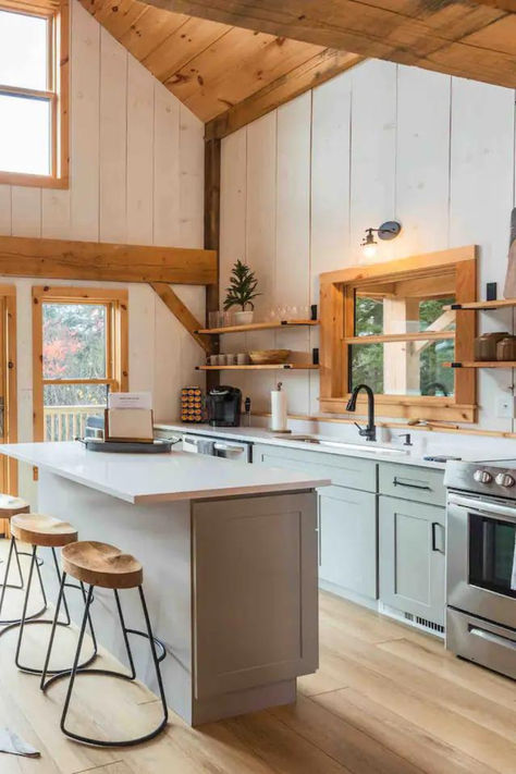 Kitchen of a post and beam cabin with light blue wooden cabinets, white painted wood walls, a white marble top island, stools with wooden seats, and a chrome oven. Modern Cozy Cabin Interior, Rustic Beach Cabin, Open Concept Cabin, Beach Cabin Interior, Post And Beam Cabin, Vermont Cabin, Fern House, Southern Vermont, One Room Cabin